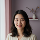 Close-up portrait of a smiling young Chinese woman with a friendly, trustworthy expression against a blurred lilac background