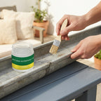 A person applying transparent waterproof glue with a brush to a cracked gutter on a slate blue and cream-toned patio.